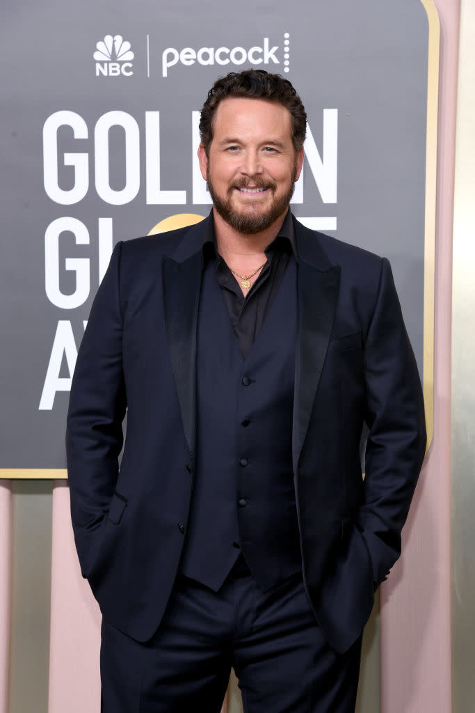 Man in a dark suit on a red carpet at an awards event, smiling