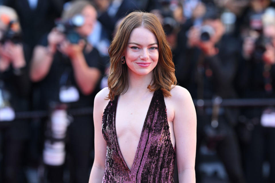 A woman on the red carpet in a plunging sequin gown, smiling at the camera