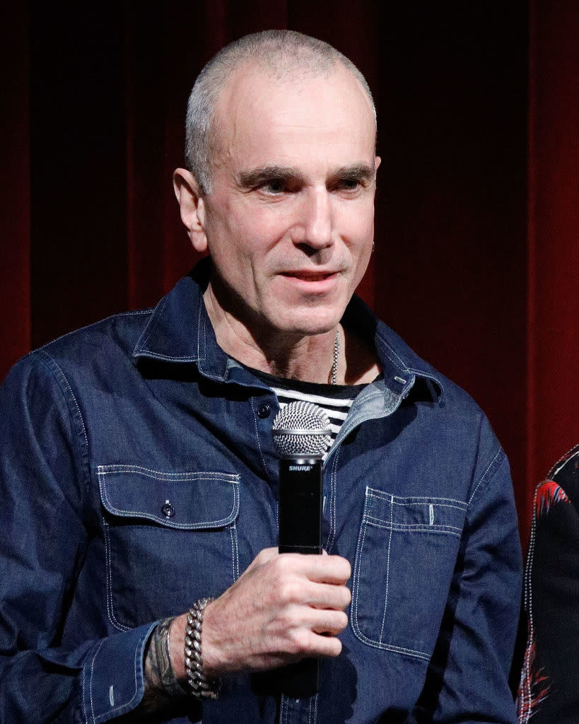 A person holding a microphone, wearing a denim jacket over a striped shirt, speaking at an event